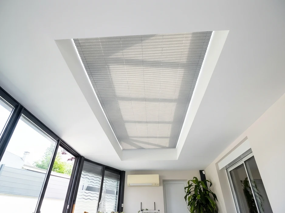 Verrière de toit intérieure équipée d'un store plissé motorisé en tissu translucide gris, intégré dans un faux-plafond blanc à caisson