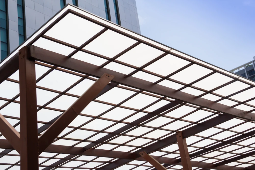 Scène extérieure urbaine montrant une pergola moderne avec structure métallique et panneaux translucides installée devant un immeuble de bureaux contemporain