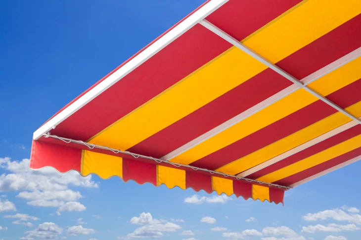 Scène extérieure avec store banne déployé sous ciel bleu nuageux