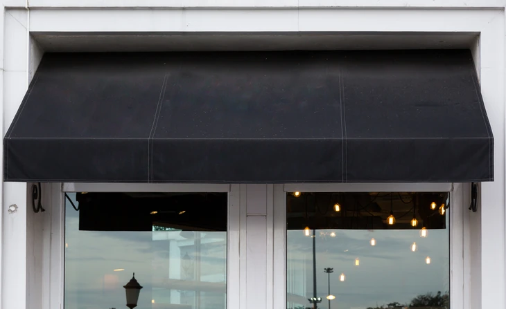 Façade commerciale avec grande baie vitrée à double vantaux et store banne noir déployé