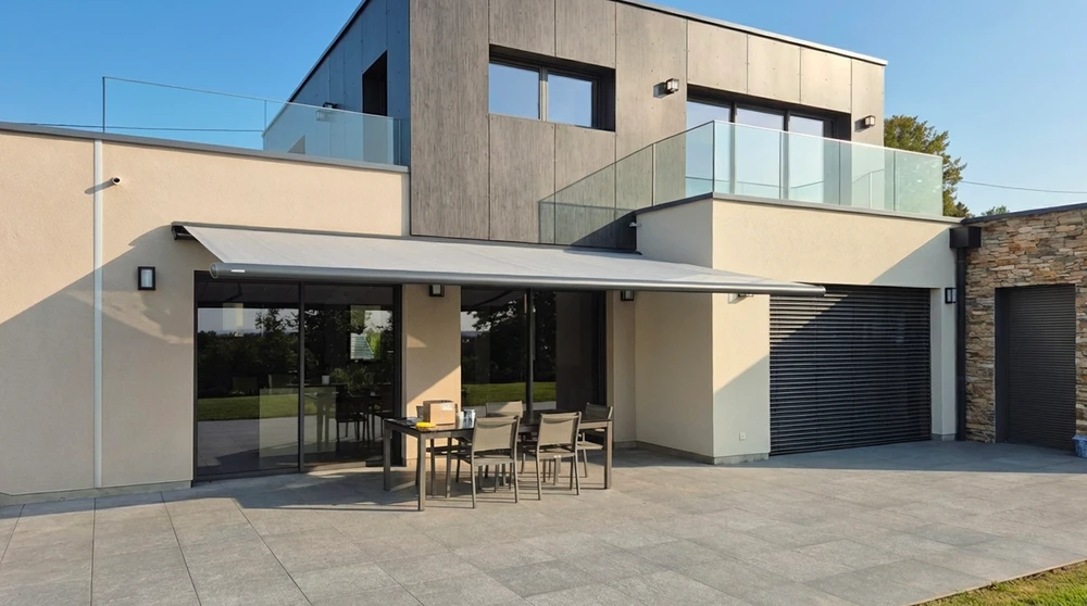 Terrasse extérieure d'une villa contemporaine avec store banne motorisé déployé, toile grise imperméable sur structure aluminium anthracite