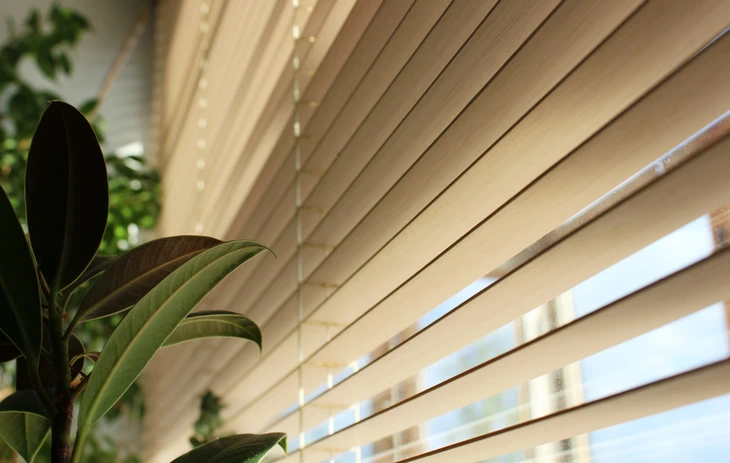 Intérieur résidentiel avec store vénitien en bois naturel partiellement ouvert laissant filtrer la lumière naturelle