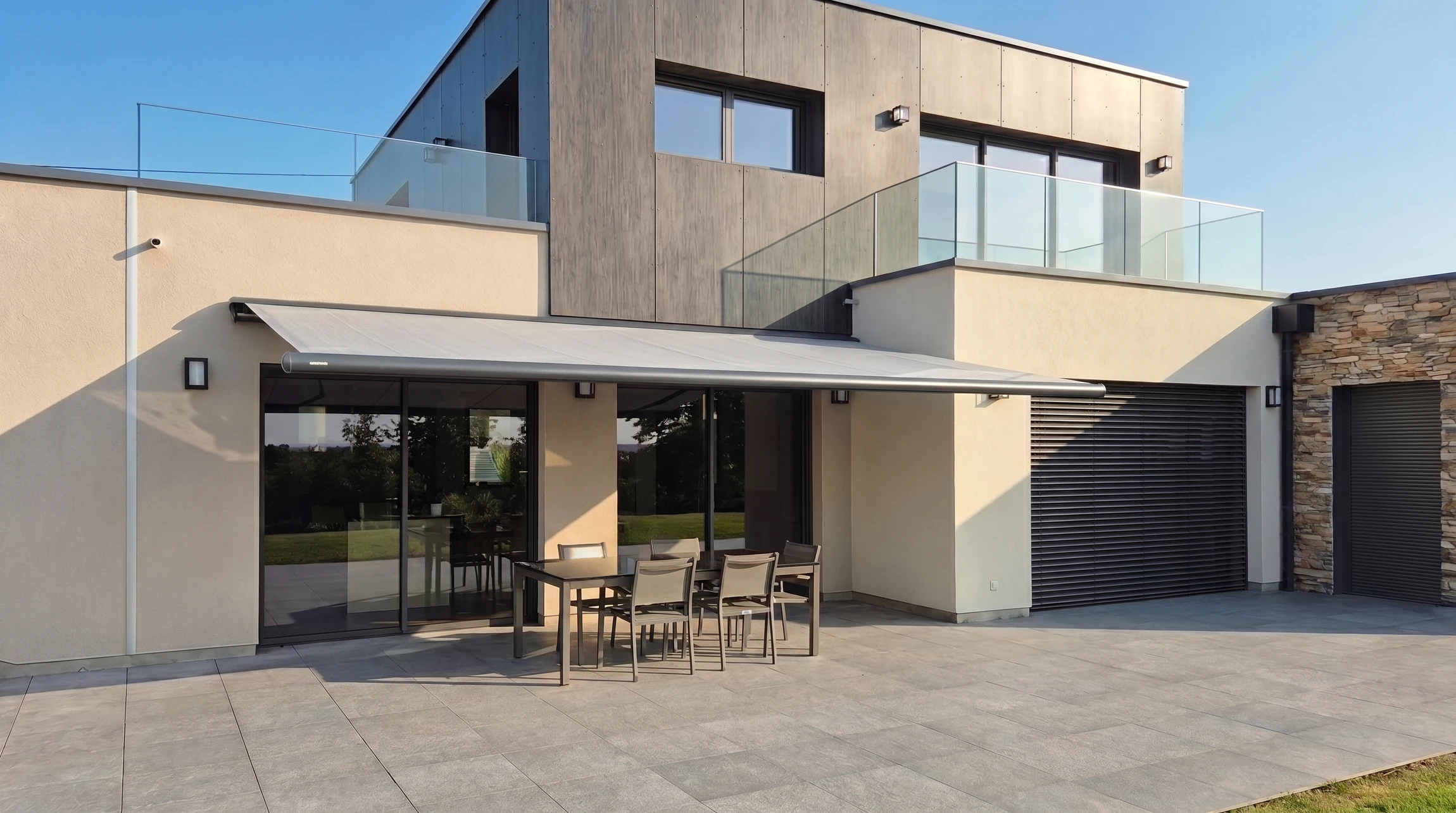 Technicien en tenue bleue installant un store banne rétractable sur la terrasse d'une maison résidentielle