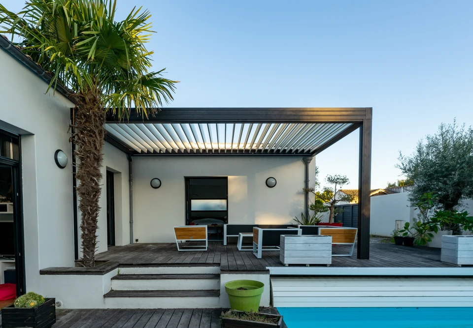 Extérieur résidentiel moderne avec pergola bioclimatique à lames orientables installée devant une maison contemporaine blanche