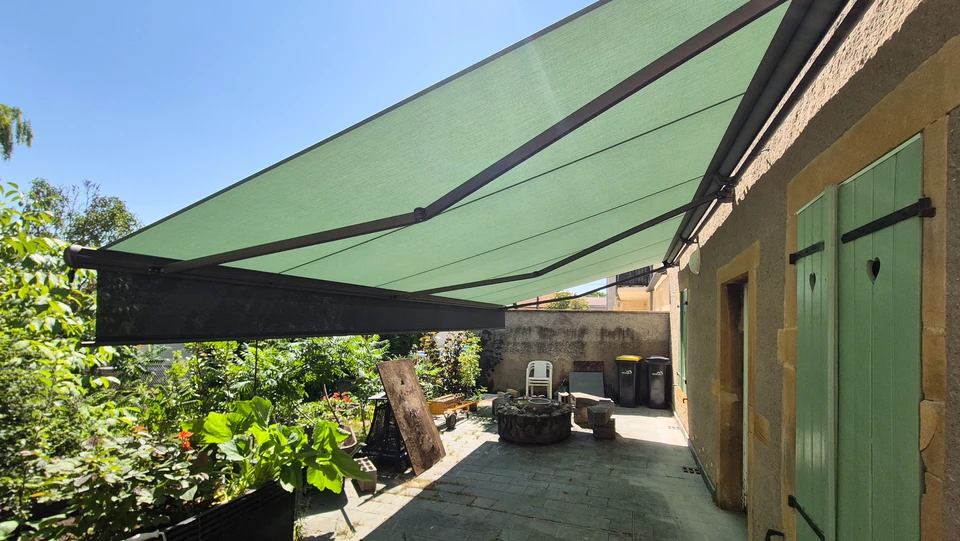 Scène extérieure montrant une pergola bioclimatique moderne à lames orientables installée contre une façade résidentielle contemporaine