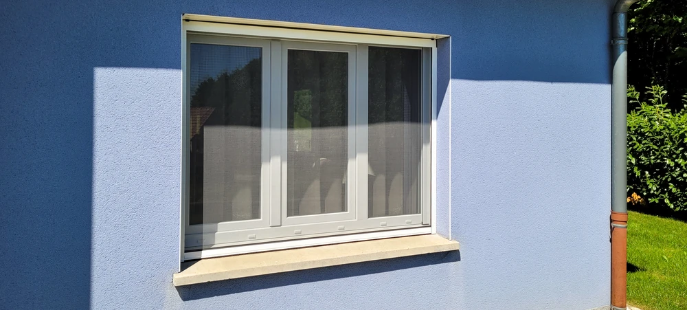 Store vénitien en bois clair, lames horizontales inclinées laissant filtrer la lumière naturelle d'une fenêtre
