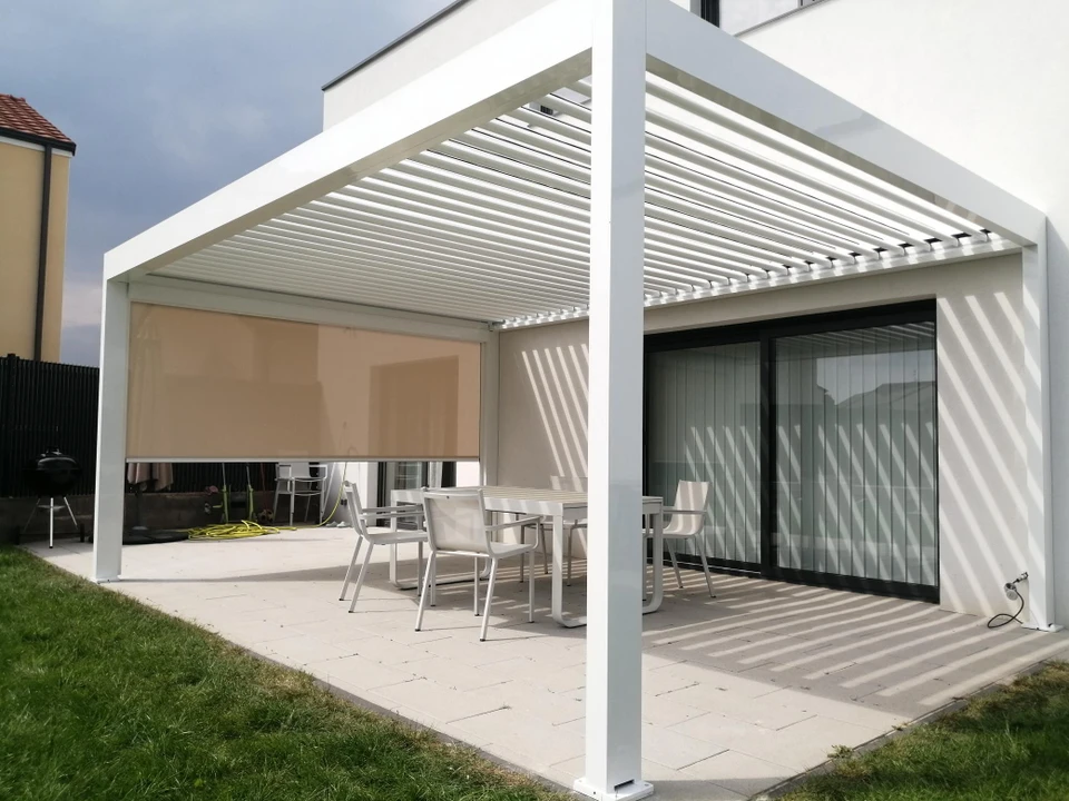 Scène extérieure montrant une pergola bioclimatique moderne à lames orientables installée contre une façade résidentielle contemporaine